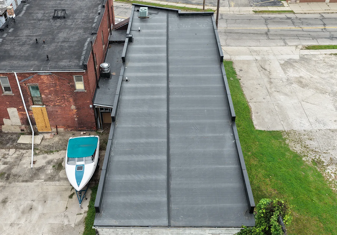 After: a long commercial flat roof, worn and patched before, a new seamed membrane after